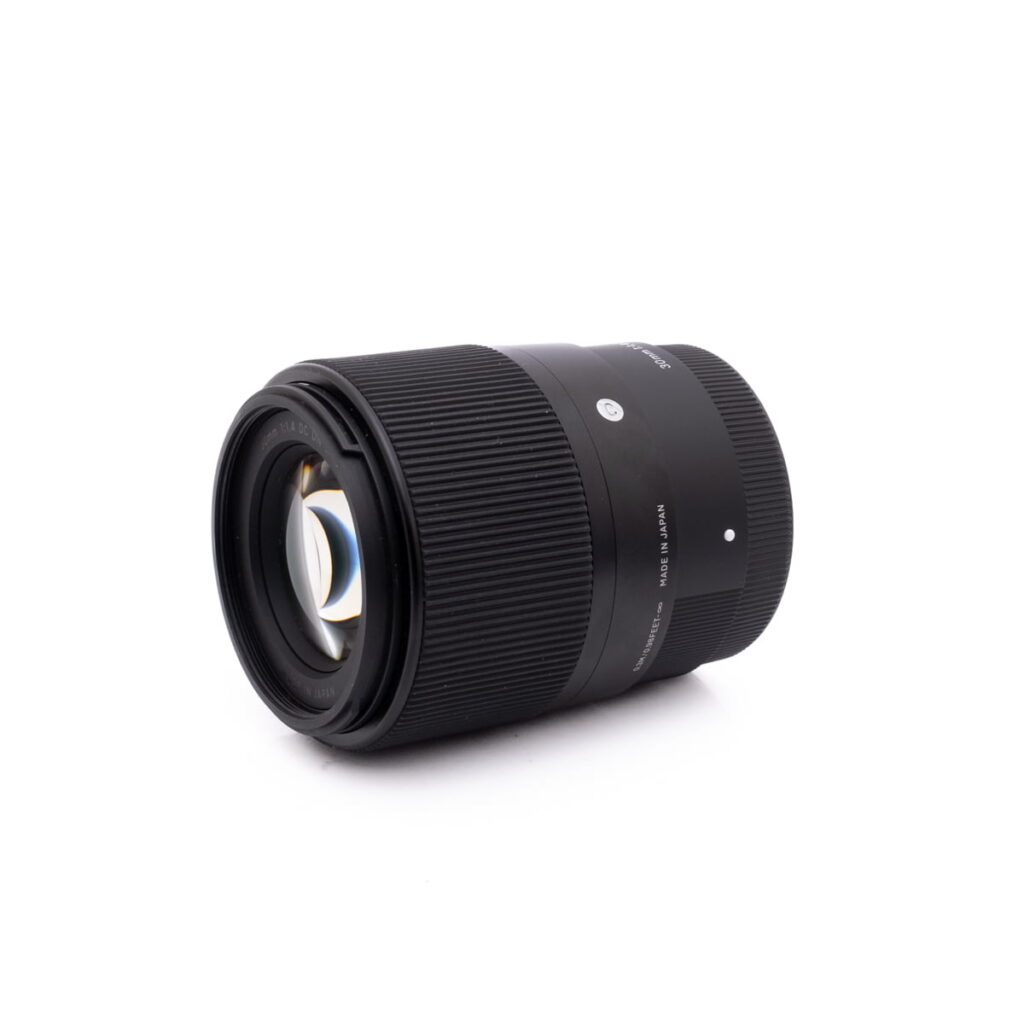 Sigma 30mm f1.4 SonyE-2 Sigma 30mm f/1.4 DC DN Sony E - Käytetty musta kameran objektiivi, jossa on uurrettu tarkennusrengas ja näkyvät lasielementit, on esillä valkoisella pohjalla, hieman sivulle kallistettuna.
