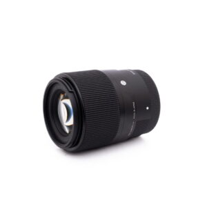 Sigma 30mm f1.4 SonyE-2 Sigma 30mm f/1.4 DC DN Sony E - Käytetty musta kameran objektiivi, jossa on uurrettu tarkennusrengas ja näkyvät lasielementit, on esillä valkoisella pohjalla, hieman sivulle kallistettuna.