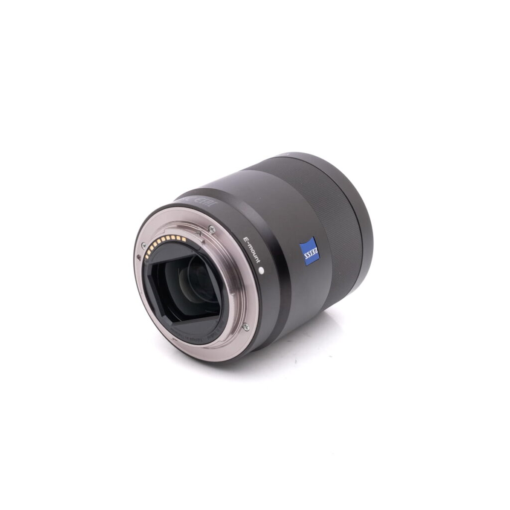 Sony-55mm-f1.8-3 Sony FE Sonnar T* 55mm f/1.8 ZA - Käytetty -objektiivi on kuvattu kyljellään, ja siinä on metallinen kiinnitys, elektroniset kontaktit, takaelementti ja Zeissin tuotemerkki valkoisella taustalla.