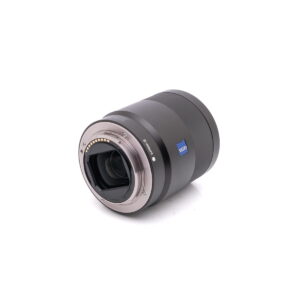 Sony-55mm-f1.8-3 Sony FE Sonnar T* 55mm f/1.8 ZA - Käytetty -objektiivi on kuvattu kyljellään, ja siinä on metallinen kiinnitys, elektroniset kontaktit, takaelementti ja Zeissin tuotemerkki valkoisella taustalla.