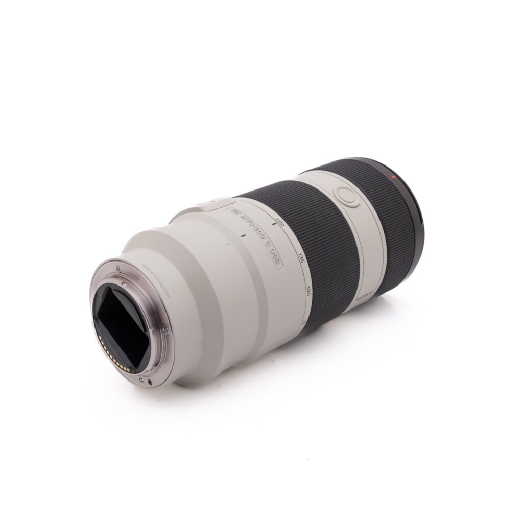 Fujinon XF 50-140mm f/2.8 OIS WR - Käytetty -objektiivi, jossa on valkoinen ja musta runko, on kuvassa kyljellään siten, että kiinnityspää osoittaa eteenpäin valkoista taustaa vasten.