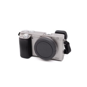 Hopea Sony a6000 (SC 470, K4.5) - Käytetty APS-C peilitön kamera, jossa on musta kahva, objektiivin kiinnityssuoja ja musta hihna kiinnitettynä, valkoisella taustalla.