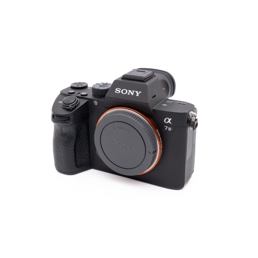 Sony-A7III-121-1 Musta Sony A7 III - Käytetty peilitön kamera, jossa on rungon suojus, hieman vinossa valkoista taustaa vasten.