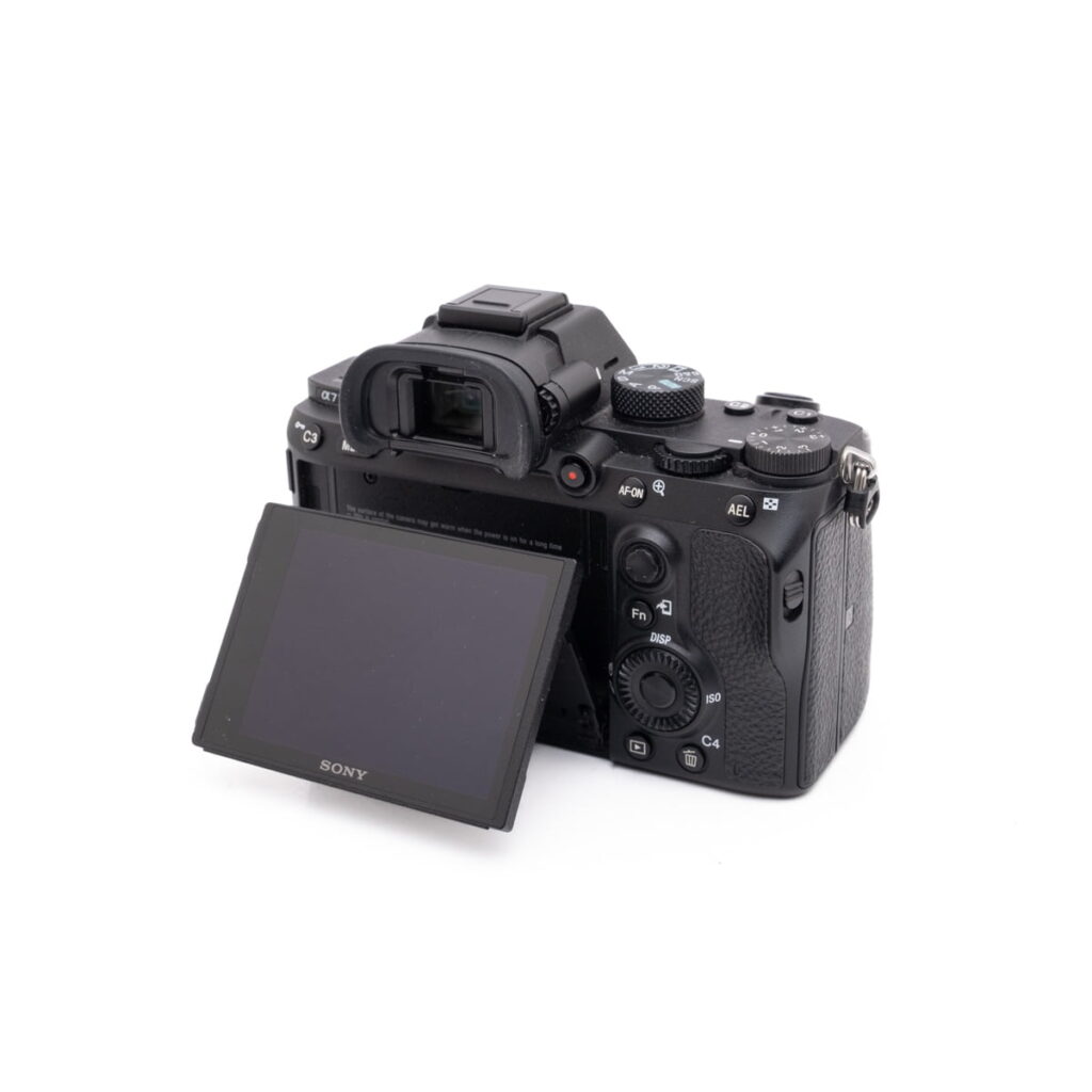 Sony-A7III-121-3 Musta Sony A7 III - Käytetty -digitaalikamera, jonka LCD-näyttö on käännetty sivulle, näyttää painikkeet ja valintakiekot valkoista taustaa vasten.