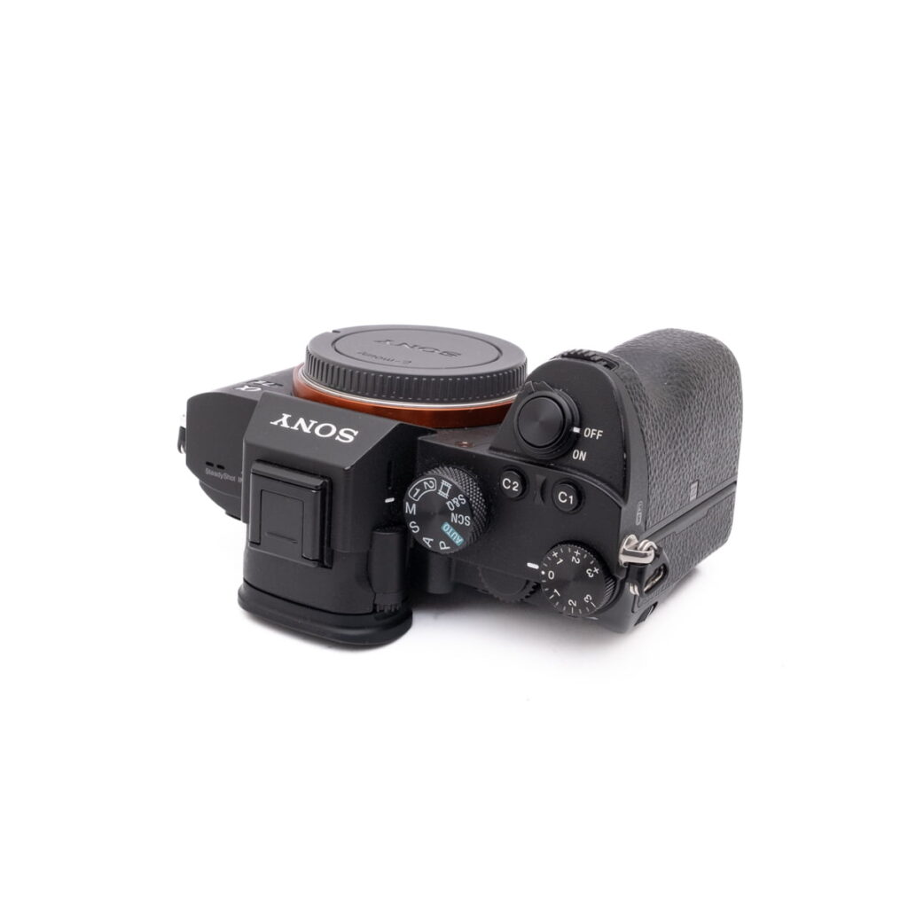 Sony-A7III-121-4 Musta Sony A7 III - Käytetty -kameran runko näkyy ylhäältä alaspäin suunnattuna, ja sen säätimet, painikkeet ja kuvioitu kahva korostuvat. Objektiivia ei ole kiinnitetty.
