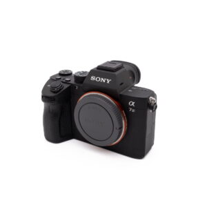 Sony-A7III-274-1 Käytetty Sony A7 III (SC 2800, Kunto K5) peilitön digitaalikamerarunko, musta ja objektiivin suojus, vinossa valkoisella taustalla.