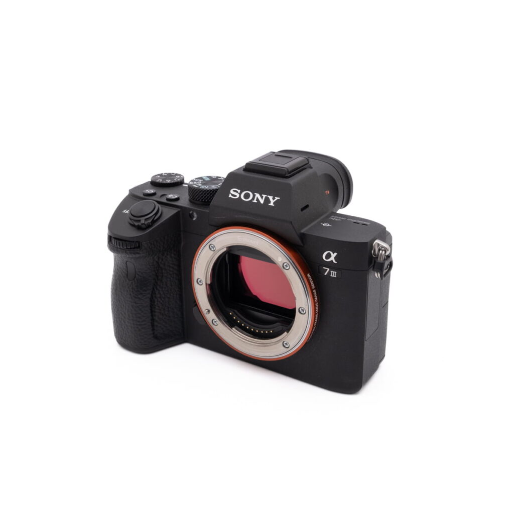 Sony-A7III-274-2 Sony A7 III (SC 2800, Kunto K5) - Käytetty peilitön kamerarunko on kuvattu oikealle, ilman objektiivia ja kenno näkyvissä valkoista taustaa vasten.