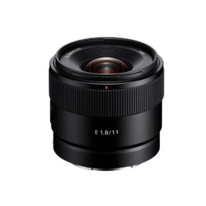Sony-E-11mm-f1.8 A Sony E 11mm f/1.8 -objektiivi, musta kameraobjektiivi, jossa leveä uritettu tarkennusrengas ja valkoinen E 1.8/11 -teksti, esillä valkoisella taustalla.