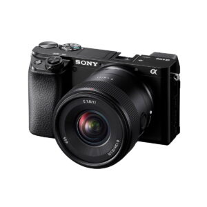 Sony-E-11mm-f1.8-6 Musta Sony Alpha 6100 -peilittömäkamera, johon on kiinnitetty Sony E 11mm f/1.8 -objektiivi, vinossa valkoista taustaa vasten.