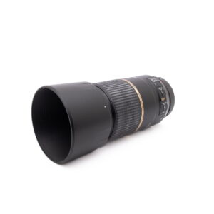 Tamron SP 90mm f/2.8 Macro Canon - Käytetty -objektiivi, musta, jossa on kuvioitu zoomausrengas sekä automaattitarkennuksen ja tärinänhallinnan kytkimet, on esillä pienessä kulmassa valkoisella taustalla.