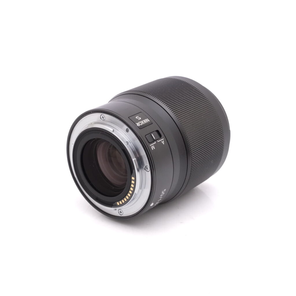 nikon-Z-50mm-f1.8-3 Nikon Nikkor Z 50mm f/1.8 S (takuu 6kk) - Käytetty objektiivi, jossa on elektroniset koskettimet ja AF/MF-kytkin, objektiivin kiinnitys ylöspäin, on sijoitettu vinosti valkoiselle taustalle.