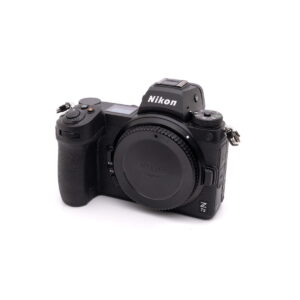 Nikon Z7 II (SC 8500, Takuu 12kk) - Käytetty peilitön kamerarunko mustana valkoisella pohjalla, hieman oikealle kallistettuna, suojus päässä ja ilman objektiivia.