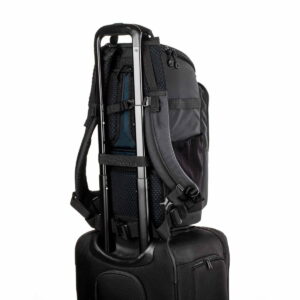 Tenba-axis V2-16L-6 The Tenba Axis V2 16L camera backpack is securely attached to the handle of the black roller bag for easy transport. The background is plain white.