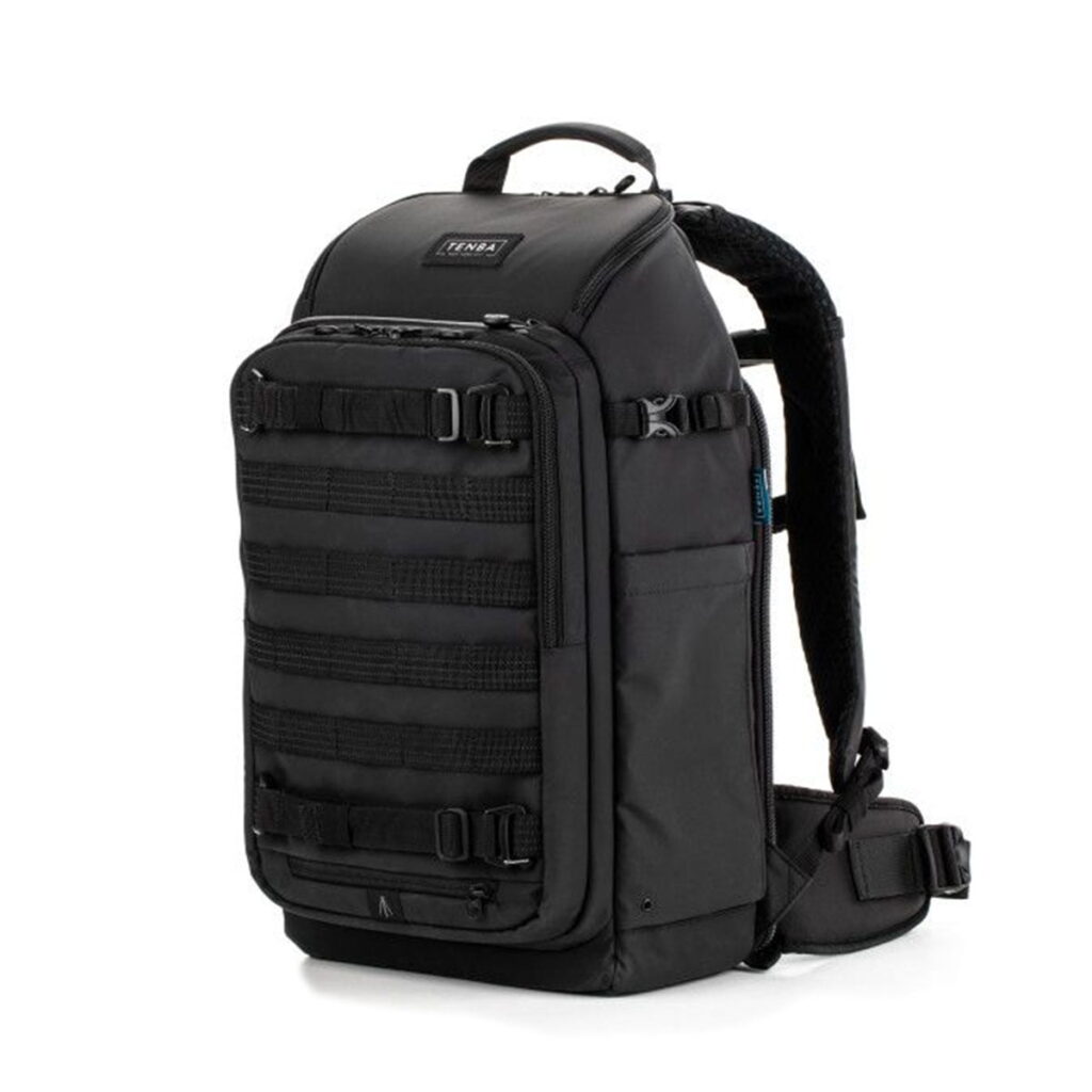 Tenba-axis-V2-20L Tenba Axis V2 20L Backpack -kamerareppu on musta taktisen tyylin reppu, jossa on useita etuhihnoja, sivutaskut ja pehmustetut olkahihnat, jotka näkyvät pystyasennossa valkoisella pohjalla.