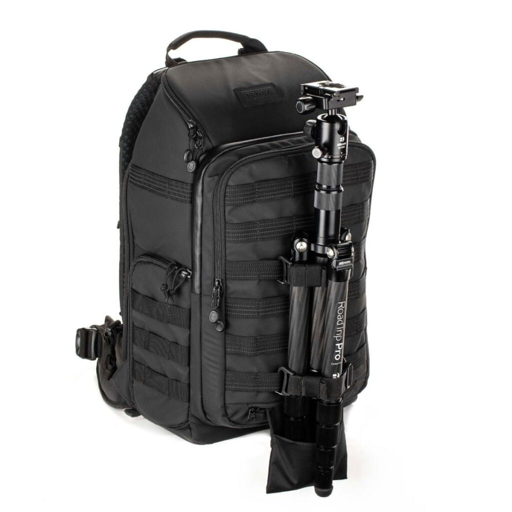 Tenba-axis-V2-20L-2 Pystyssä seisovassa Tenba Axis V2 20L -reppu -kamerareppu -kamerareppu sisältää useita vetoketjullisia lokeroita ja mustan jalustan, joka on kiinnitetty sivuun säädettävillä hihnoilla ja pienellä taskulla.