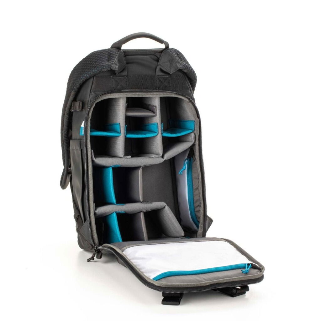 Tenba-axis-V2-20L-3 Tenba Axis V2 20L Backpack -kamerareppu on musta reppu, jonka vetoketju aukeaa edestä ja paljastaa pehmustetut, säädettävät lokerot kameravarusteiden tai elektroniikan järjestämiseen ja suojaamiseen. Sisätiloissa on harmaita ja tiilenpunaisia korostuksia.
