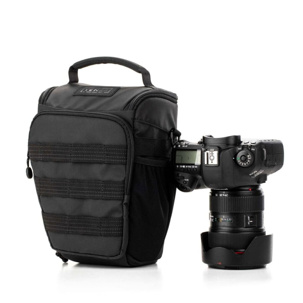 Tenba-axis V2-4L-4 The Tenba Axis V2 4L Top Loader camera bag with handle sits next to a professional DSLR camera with a large lens and lens cover, both against a white background.
