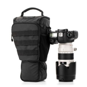 Tenba-axis V2-4L-5 A black DSLR camera with a large white telephoto lens stands upright next to the Tenba Axis V2 4L Top Loader, a padded black camera case with zippers and top handle.