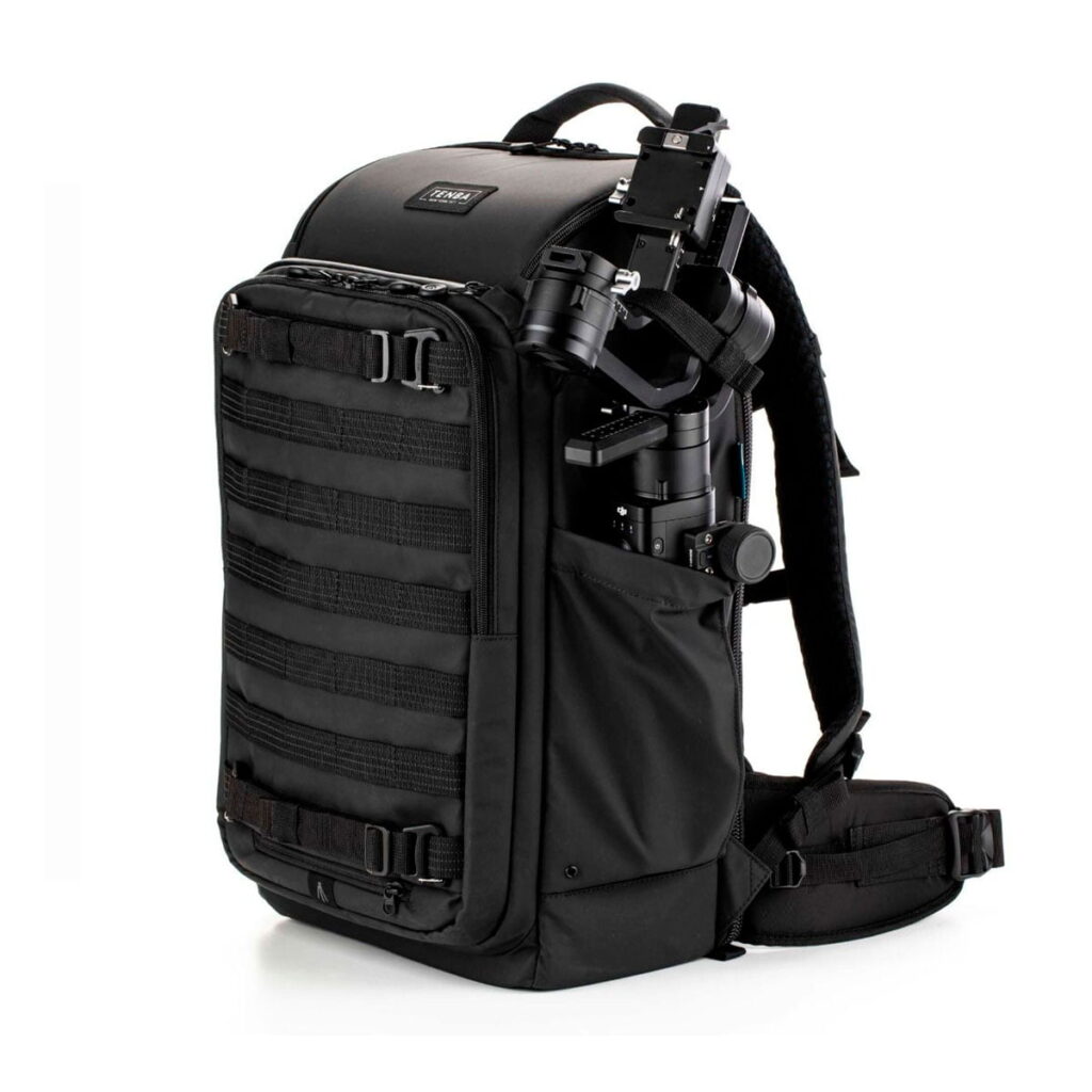 Tenta-axis V2-2 The Tenba Axis V2 24L Backpack is a black camera backpack with padded shoulder straps, side and front pockets and external straps. The picture shows the camera flash in one of the side pockets against a white background.