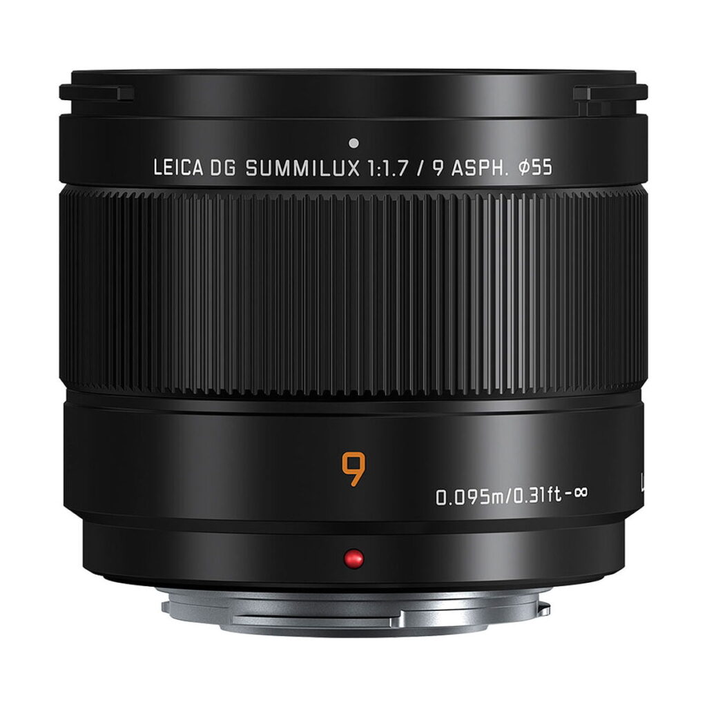 Panasonic_-Leica_DG_Summilux_9mm_f_1_7_ASPH Panasonic Leica DG Summilux 9mm F/1.7 ASPH -objektiivi on esitetty mustana, jossa on uurrettu tarkennusrengas, valkoiset ja oranssit merkinnät sekä punainen kohdistuspiste valkoista taustaa vasten.