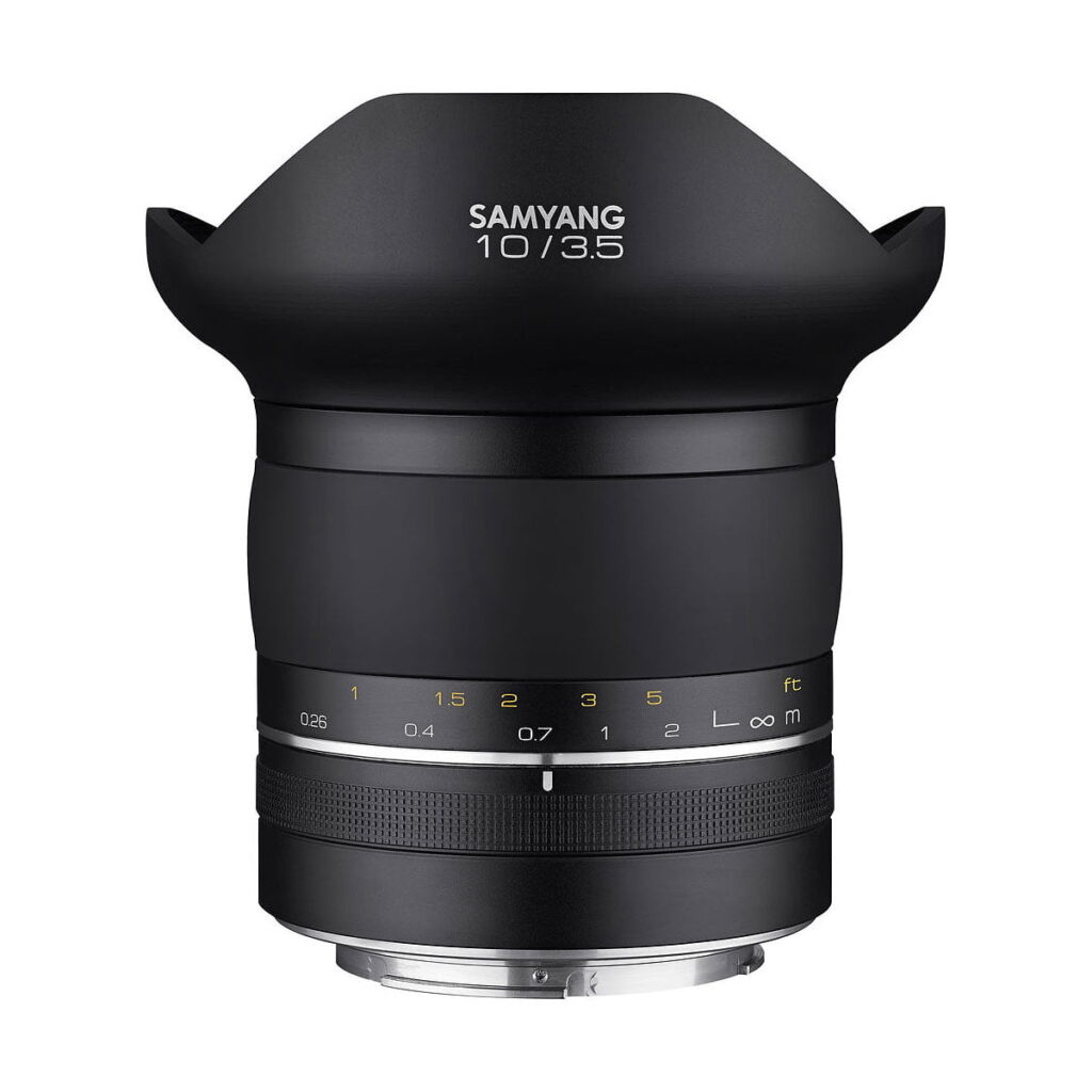 Samyang_10mm_f_3_5_XP_001 Samyang XP 10mm f/3.5 - Canon EF -objektiivissa on musta mattapinta, terälehden muotoinen huppu, tarkennusetäisyysmerkinnät ja metallinen kiinnike valkoista taustaa vasten.