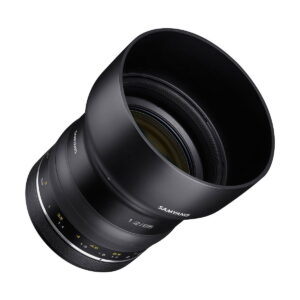 Samyang_XP_85mm_f_1_2_003 Samyang XP 85mm f/1.2 for Canon EF on musta kameraobjektiivi, jossa on keltaiset ja valkoiset merkinnät, leveä huppu ja aukkomerkinnät, kuvattuna kulmassa valkoisella pohjalla.