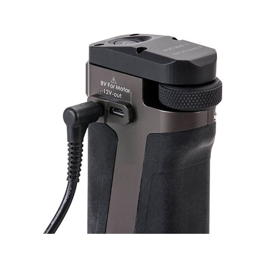 Tilta_Sidehandle_Power_Cabe_002 Lähikuva Tilta BMPCC 4K Side Handle to BMPCC 4K Camera Power Cable -johdosta, joka on kytketty mustan laitekahvan 8V-moottorin ja 12V-out-portteihin valkoista taustaa vasten.