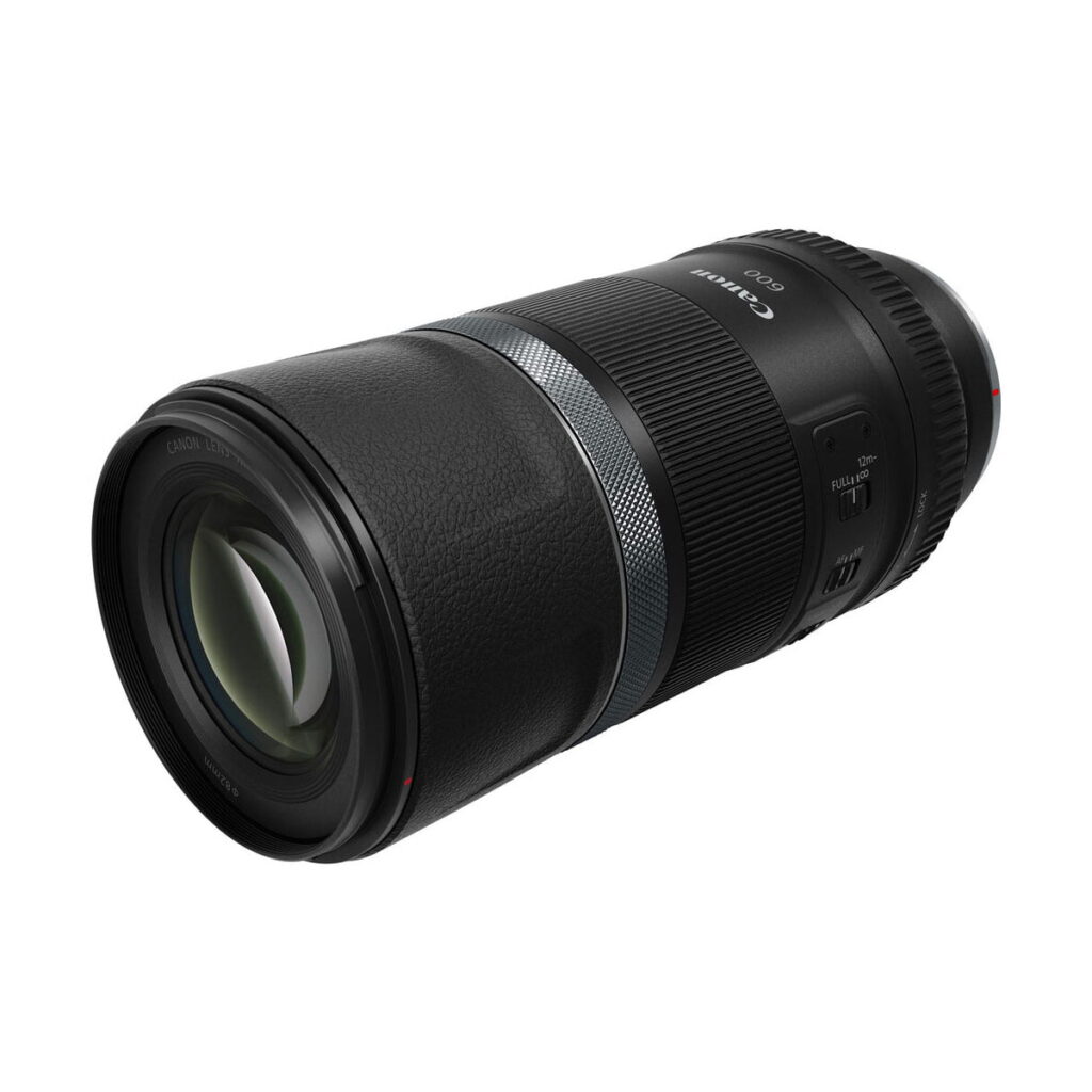 canon_rf_600mm_is_stm_02 A Canon RF 600mm f/11 IS STM lens, black construction, against a white background. The lens has a milled grip, focus adjustment ring, detailed markings and a switch on the side.