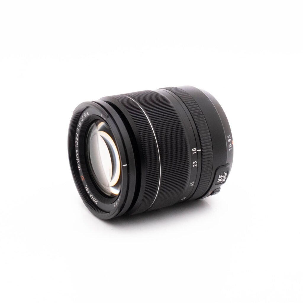 Fujifilm 18-55mm-2 Fujifilm X-S10 (SC 1189)- Käytetty on kuvattu kulmassa valkoisella taustalla, ja siinä on kuvioidut säätörenkaat, näkyvät lasielementit ja tarkennusmerkinnät.