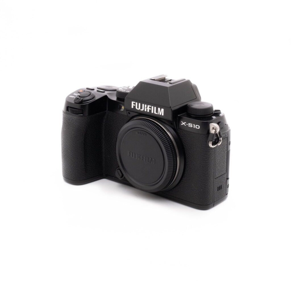Fujifilm X-S10-1 Fujifilm X-S10 (SC 1189)- Käytetty digitaalikamera näkyy valkoisella taustalla. Mustaan kameraan ei ole kiinnitetty objektiivia, objektiivin kiinnityssuojus on paikallaan ja mallin nimi näkyy selvästi rungossa.