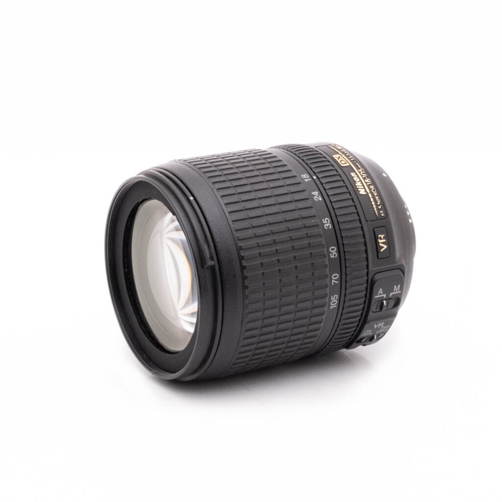 Nikkor 18-105-2 Canon EF 100-400mm f/4.5-5.6 L IS II USM - Käytetty musta DSLR-kameran zoom-objektiivi, jossa on kuvioitu kahva ja säätörenkaat ja jossa näkyy näkyvä objektiivilasi, näkyy valkoisella pohjalla.