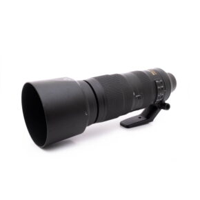 Nikkor 200-500mm-1 Nikon AF-S Nikkor 200-500mm f/5.6E ED VR - Käytetty teleobjektiivi, musta, vastavalosuoja ja jalustakiinnitys, näkyy valkoisella pohjalla hieman vasemmalle suunnattuna.