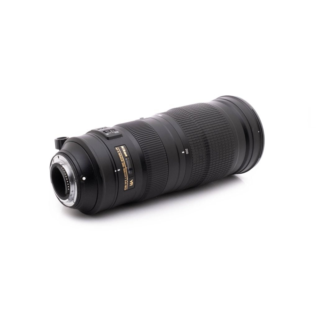 Nikkor 200-500mm-3 Nikon AF-S Nikkor 200-500mm f/5.6E ED VR - Käytetty teleobjektiivi, jossa on kultaiset ja valkoiset merkinnät, on kuvattu kulmassa valkoisella taustalla, ja siinä näkyy objektiivin kiinnitys ja näkyvät tuotemerkin merkinnät.