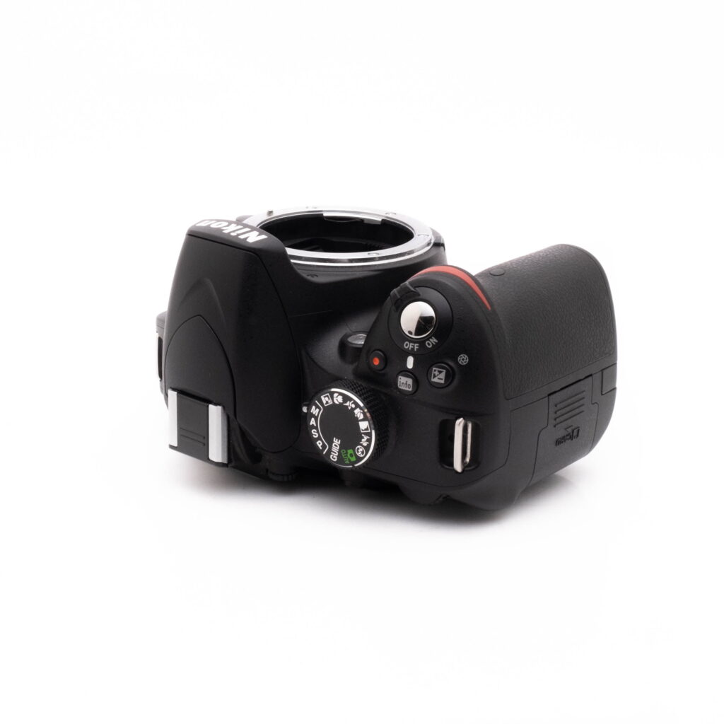 Nikon D3200 kit-5 Nikon D3200 + 18-55mm (SC 3378) - Käytetty näytetään ylhäältäpäin valkoisella pohjalla, jossa näkyvät sen painikkeet, säätimet ja objektiivin kiinnitys ilman kiinnitettyä objektiivia.