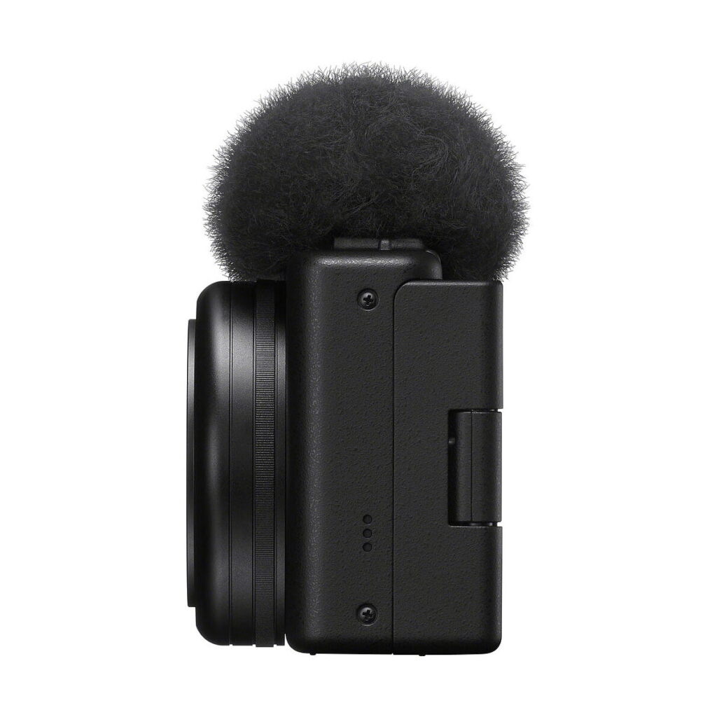 Sony_ZV-1F_006 Sivukuva Sony ZV-1F -kompaktikamerasta, kompaktista mustasta digitaalikamerasta, jossa on objektiivi ja sumea tuulisuoja äänen kohinan vähentämiseksi, eristettynä valkoiselta taustalta.