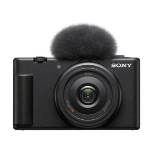 Sony_ZV-1F_008 Etukuva mustasta Sony ZV-1F -kompaktikamerasta, jossa on suuri pyöreä linssi ja siihen kiinnitetty sumea tuulilasi, joka on suunniteltu vähentämään melua äänitallennuksen aikana.