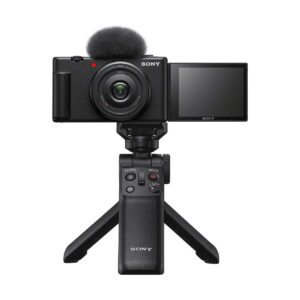 Sony_ZV-1F_009 Musta Sony ZV-1F -kompaktikamera, jossa on ulosvedettävä näyttö ja yläosan mikrofoni, asennettuna kompaktin Sonyn jalustakahvan varaan, valkoista taustaa vasten.