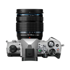 om-5_12-45mm_hopea_01 Yläkuvassa OM SYSTEM OM-5 + 12-45mm f/4 hopea, hopeanvärinen ja musta digitaalikamera, jossa on suuri zoom-objektiivi, M.Zuiko Digital 12-45mm 1:4, ja jossa näkyy säätöpyörät, painikkeet ja digitaalinäyttö.