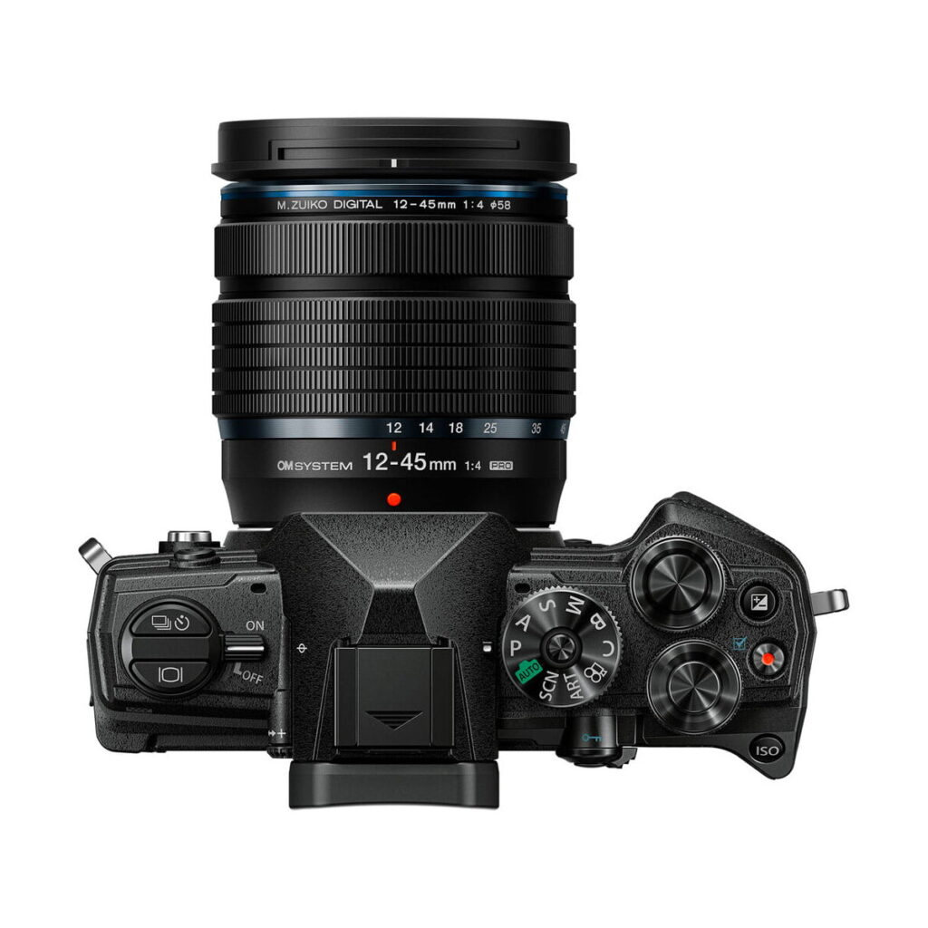 om-5_12-45mm_musta_01 OM SYSTEM OM-5 + 12-45mm f/4 musta kameran ylhäältä katsottuna, jossa on suuri zoom-objektiivi, jossa on merkintä "M.Zuiko Digital 12-45mm 1:4", useita säätöpyöriä, painikkeita, näyttöpaneeli ja erilaisia tila-asetuksia mustassa kamerarungossa.