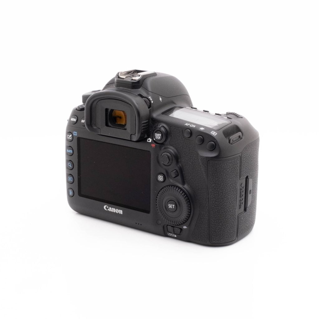 Canon 5DmkIV-3 Canon EOS 5D Mark IV (SC 23300, takuu 6kk, sis.ALV24%) - Käytetty on kuvattu takavasemmasta kulmasta, ja sen LCD-näyttö, painikkeet, valitsimet ja kuvioitu kahva korostuvat valkoista taustaa vasten.