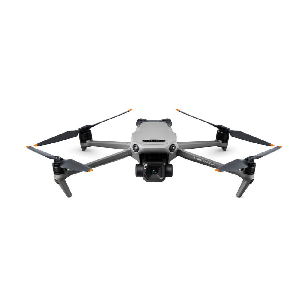 Dji_Mavic_3_Classic_001 DJI Mavic 3 Classic -lennokki, jossa on harmaa runko, neljä oranssilla kärjellä varustettua potkuria ja etukamera, näkyy valkoisella taustalla.