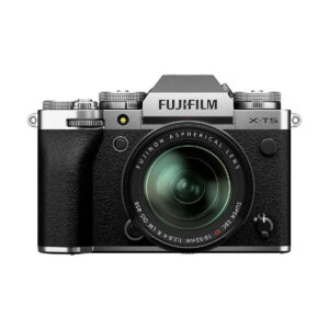 Fuji_X-T5-18-55mm_Hopea_001 Fujifilm X-T5 + XF 18-55mm f/2.8-4 R LM OIS - Hopea-kamera, jossa on hopeanvärinen ja musta runko ja kiinnitetty zoom-objektiivi, etupuolella valkoisella taustalla.