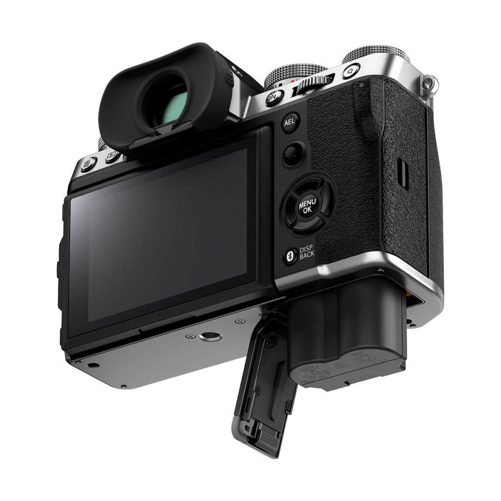 Fuji_X-T5_Hopea_003 Fujifilm X-T5 -järjestelmäkamera, hopea näkyy takaa ja alhaalta LCD-näyttö näkyvissä, akkulokero auki ja osittain irrotettu akku. Kamerassa on musta ja hopeinen runko, jossa on kuvioitu kahva.