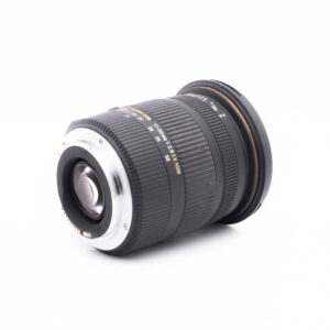 Sigma 17-50 Canon-3 Sigma DC 17-50mm f/2.8 EX HSM OS Canon EF-S - Käytetty musta DSLR-objektiivi lepää kyljellään valkoista taustaa vasten, ja siinä on näkyvissä uurteiset zoomaus-/tarkennusrenkaat, lasielementit ja metallinen kiinnityspää.