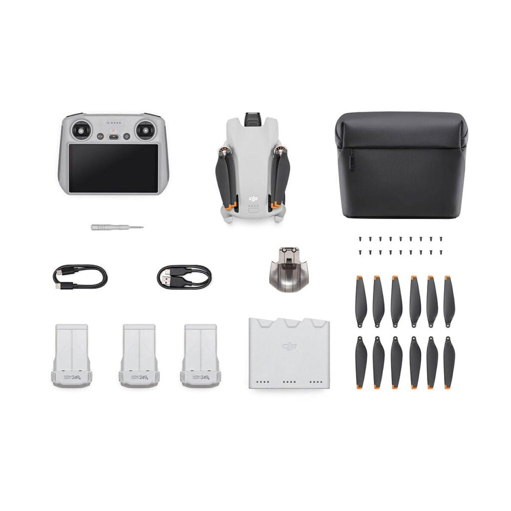 DJi_Mini_3_RC_Fly_MoreCombo_001 DJI Mini 3 + Smart Controller + Fly More Combo -yhdistelmä ylhäältä alaspäin, jossa lennokki (taitettuna), älykäs ohjain, kantolaukku, ruuvimeisseli, kaapelit, latauskeskitin, varapotkurit, akut ja ruuvit on järjestetty siististi valkoiselle taustalle.