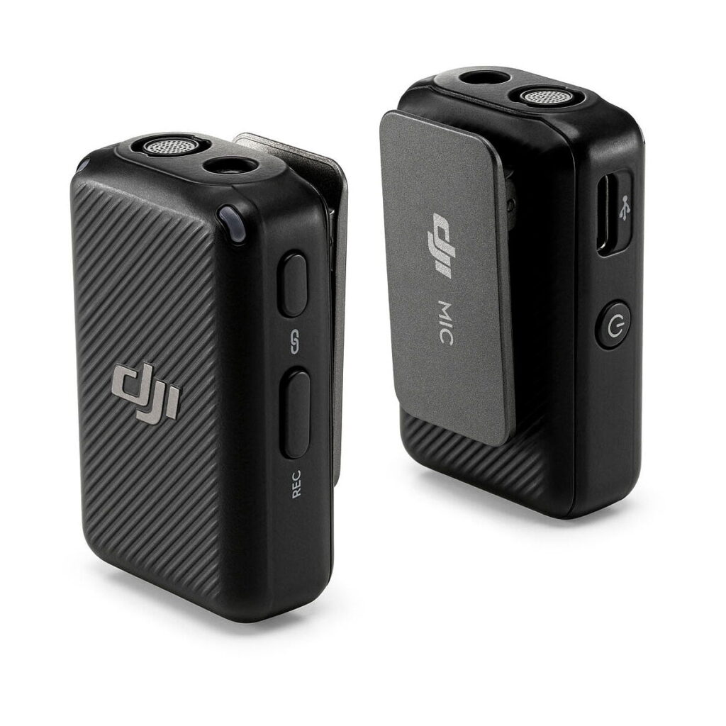 DJi_Mic_005 Kahdessa mustassa DJI Mic Dual Kit -langaton mikrofonijärjestelmä -lähettimessä on kuvioidut pinnat, sivupainikkeet ja näkyvät DJI-logot. Toisessa näkyy virtapainike ja USB-portti; toisessa on DJI MIC -merkinnällä varustettu pidike.