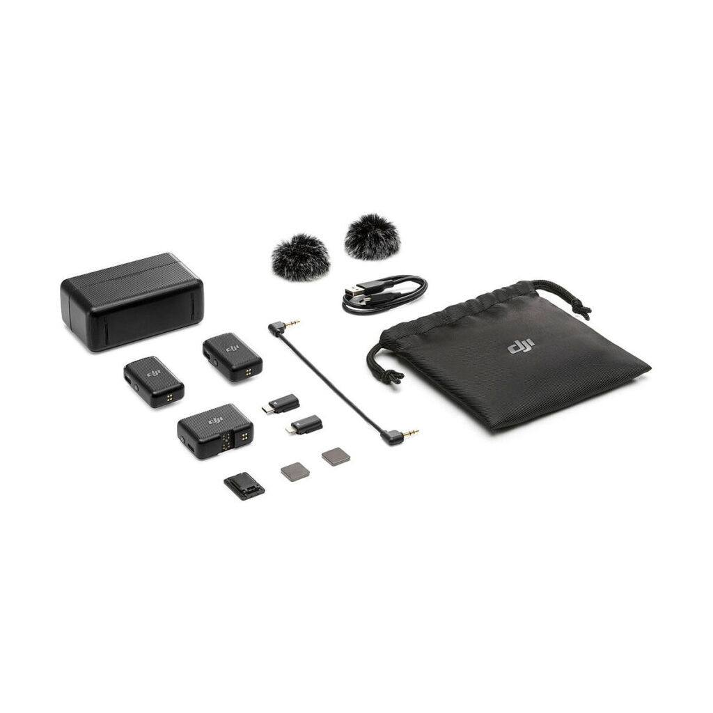 DJi_Mic_011 DJI Mic Dual Kit -langaton mikrofonijärjestelmä esillä valkoisella taustalla: kaksi lähetintä, yksi vastaanotin, tuulisuojaimet, latauskotelo, kaapelit, adapterit, microSD-kortit ja musta kiristysnyöripussi.