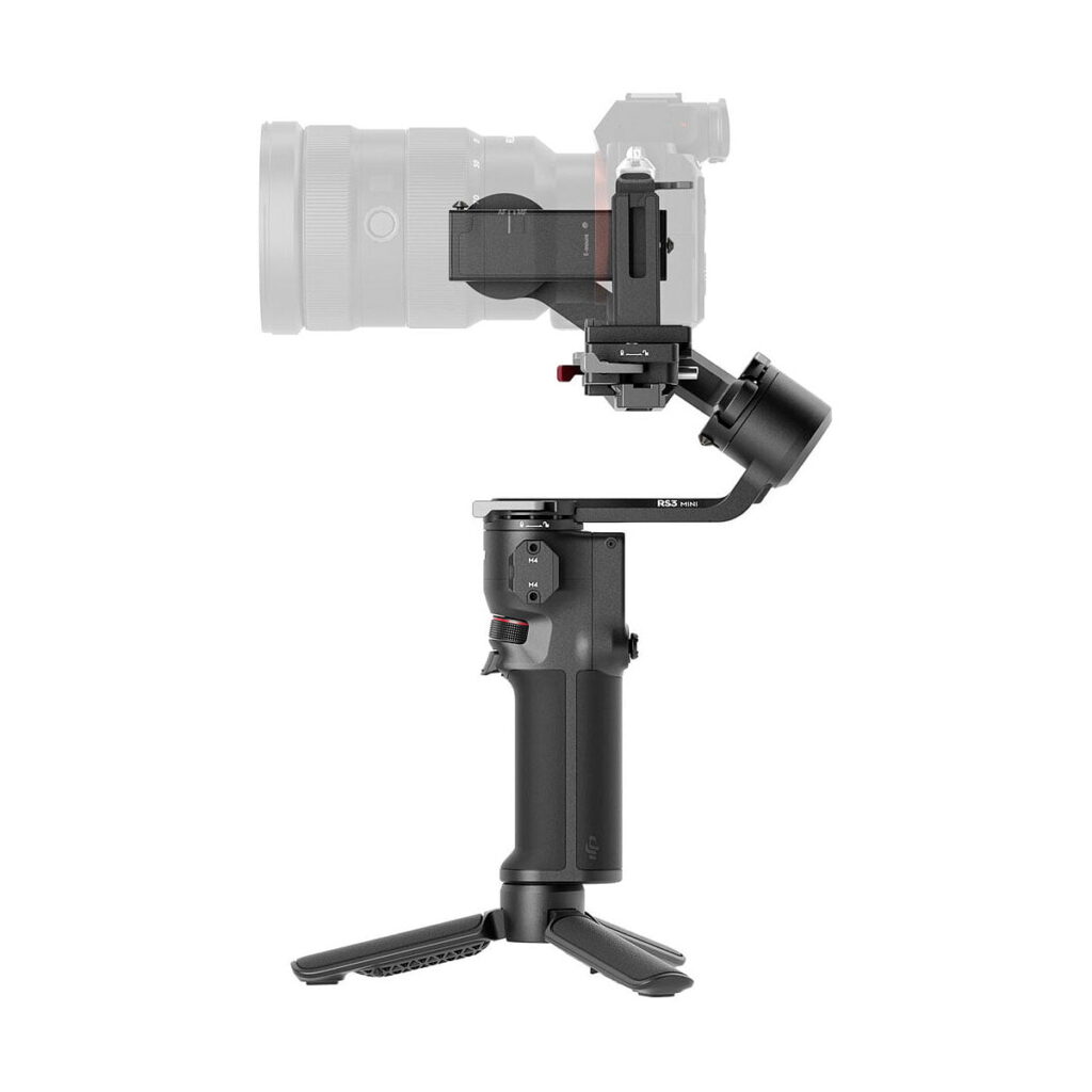 DJi_RS_3_Mini_005 The DJI RS 3 Mini gimbal, a black handheld camera gimbal stabilizer with stand, is shown holding a semi-transparent camera against a white background.