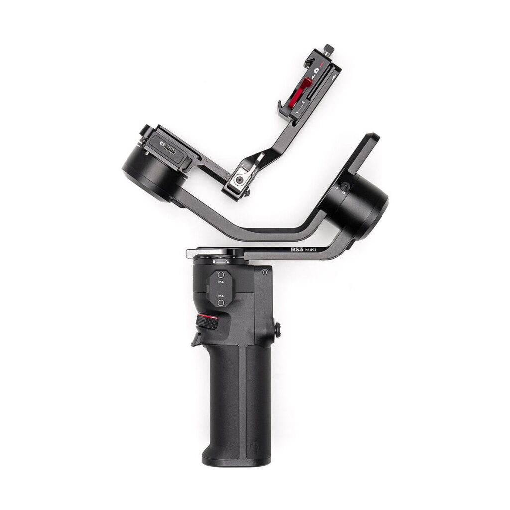 DJi_RS_3_Mini_006 The DJI RS 3 Mini gimbal is a black handheld camera stabilizer with an ergonomic handle, control buttons and an L-shaped bracket for mounting the camera, shown against a white background.