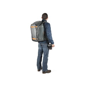 LOWEPRO Back Pack Whistler BP 350 AW II GL Grey9 Siniseen takkiin ja farkkuihin pukeutunut mies seisoo kasvot menosuuntaan, hänellä on Lowepro Whistler BP 350 AW II GL -kamerarepussa oranssit korostukset ja hänellä on kamera oikeassa kädessään.